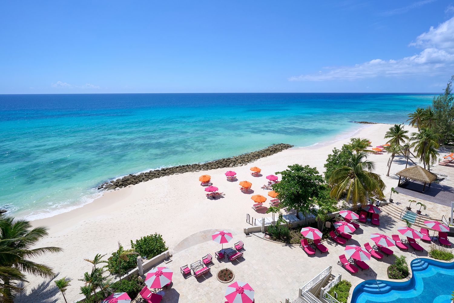 Aerial view of a tropical beach resort with turquoise water and pink beach umbrellas.