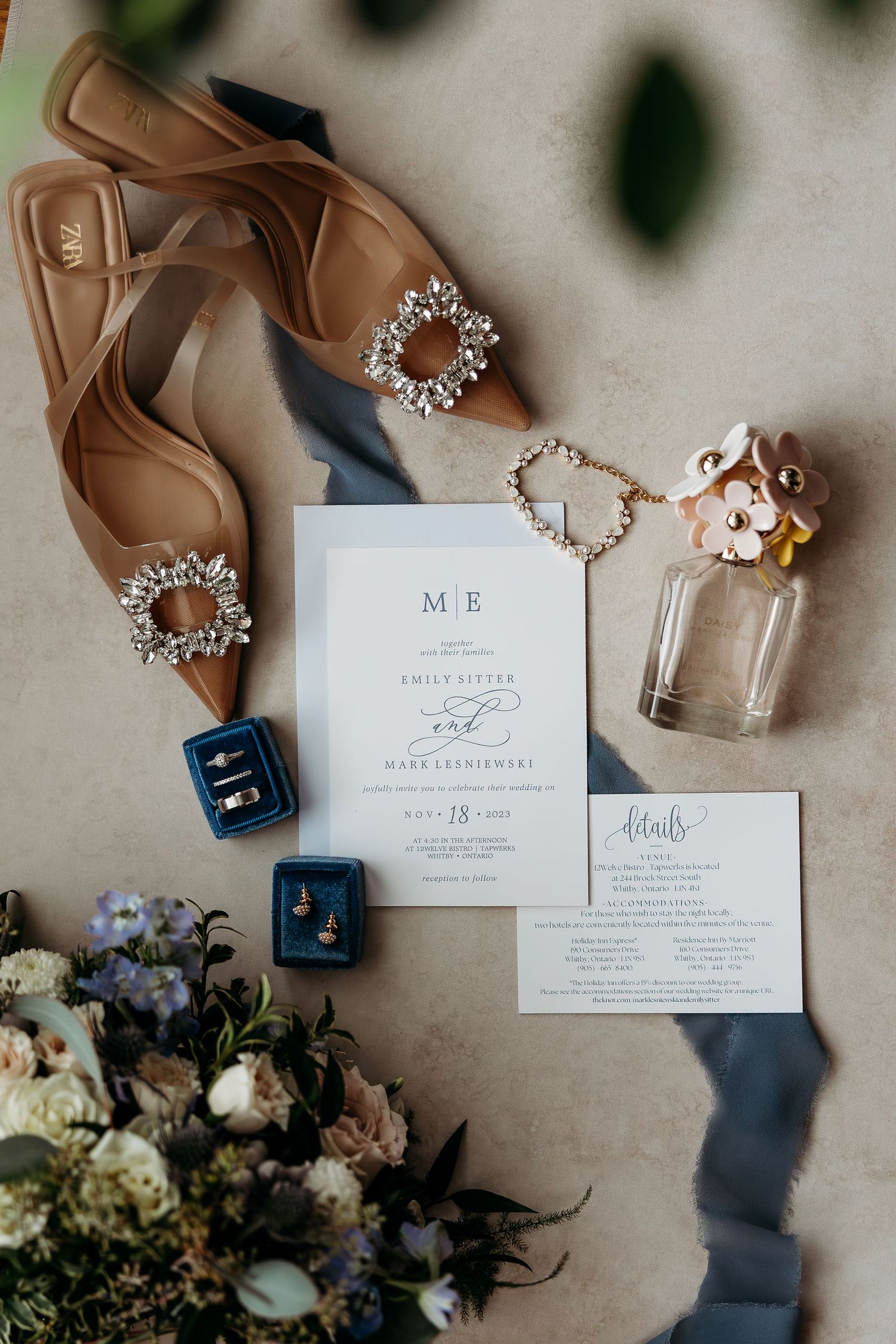 Wedding flat lay with tan shoes, jewelry, invitation suite and delicate floral details.