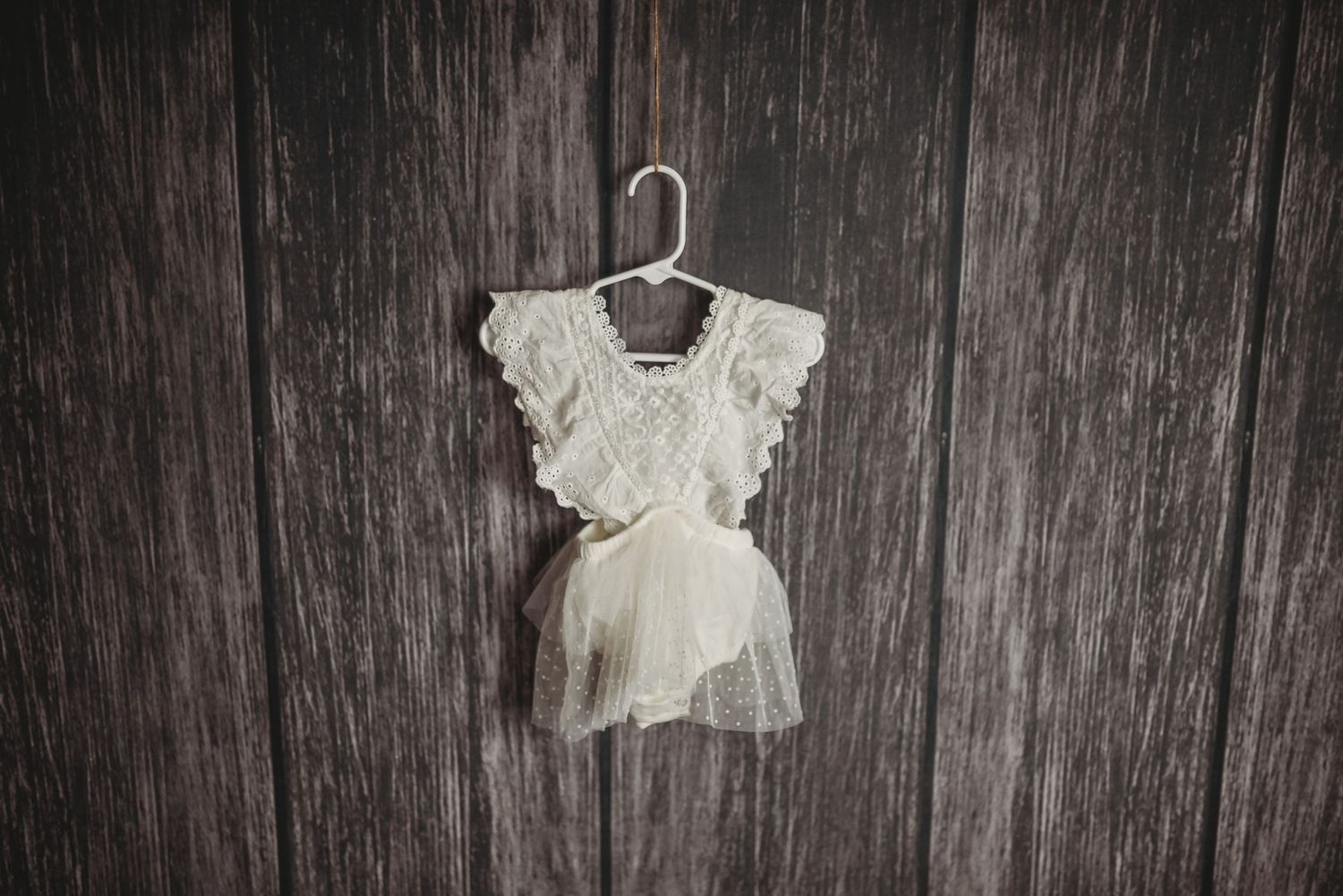 White lace baby dress with ruffled sleeves on dark wooden background.