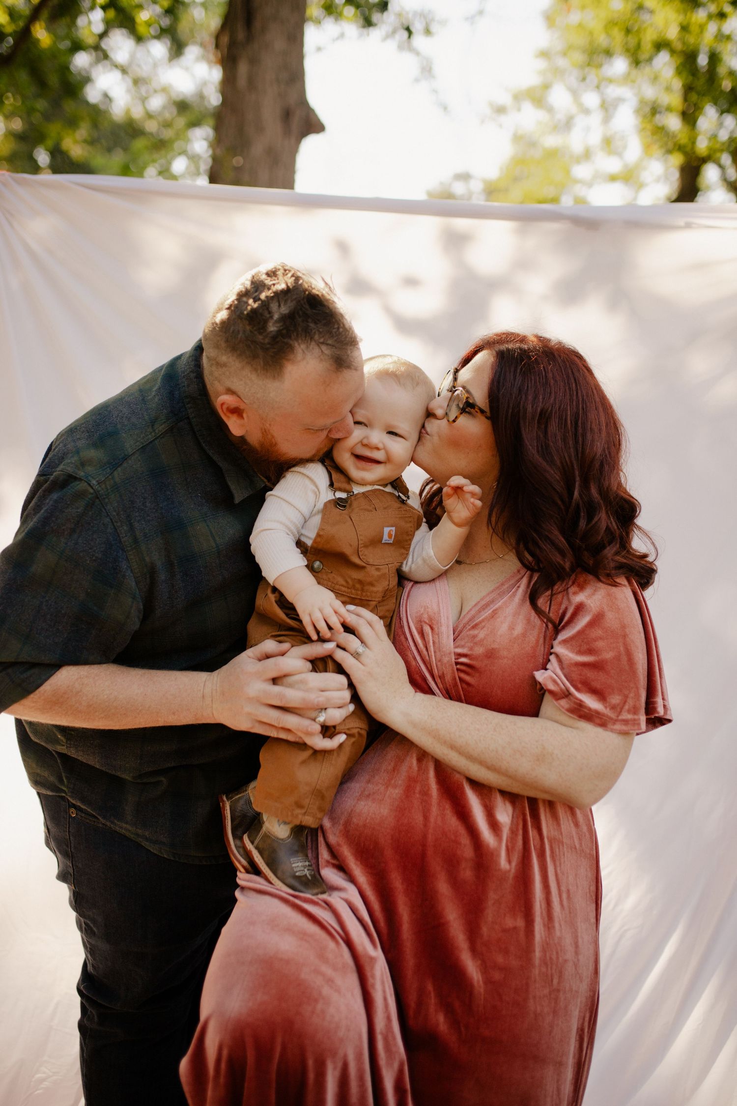 A tender family moment outdoors with a baby against a white backdrop.
