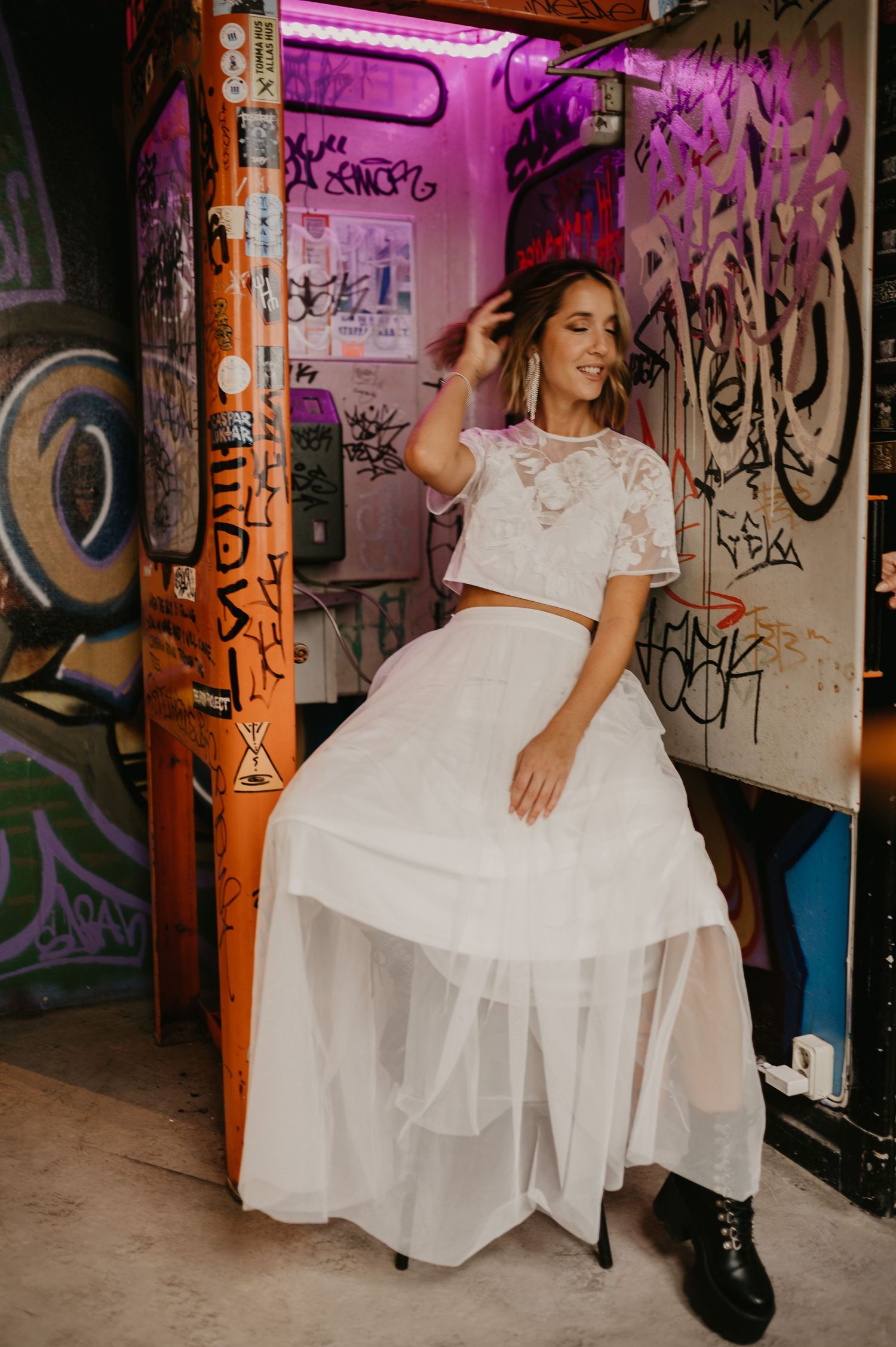 Woman in white lace crop top and tulle skirt posing in front of colorful graffiti walls.