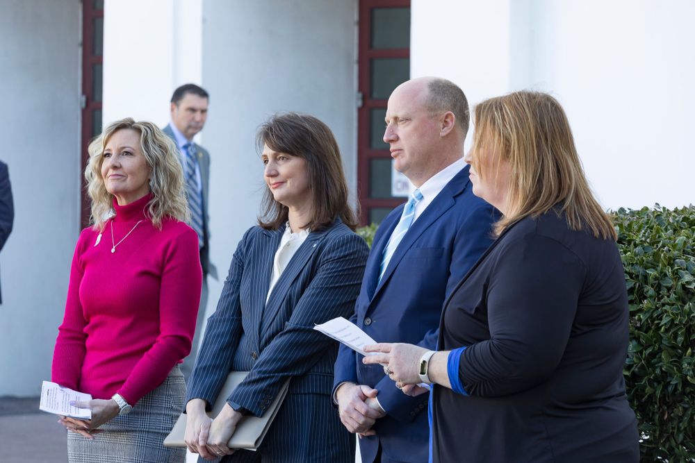 Group of presenters stand together at Educational Freedom Day event in front of white building.