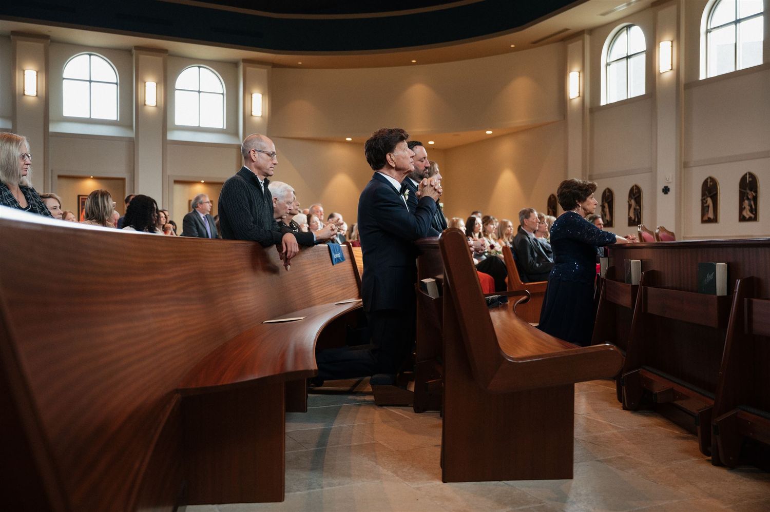 Wedding guests standing in curved wooden church pews during ceremony.