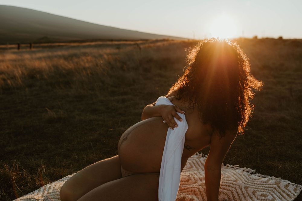 sunset hawaii maternity photoshoot flower bouquet white sheet topless sun flares at mana road in hilo, hawaii