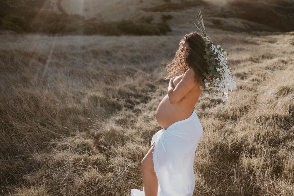 sunset hawaii maternity photoshoot flower bouquet white sheet topless sun flares at mana road in hilo, hawaii