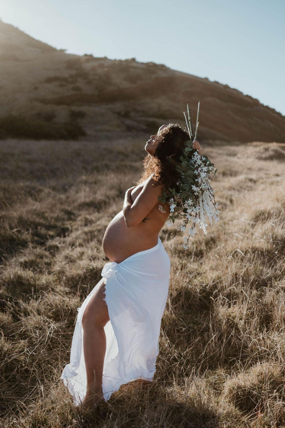 sunset hawaii maternity photoshoot flower bouquet white sheet topless sun flares at mana road in hilo, hawaii