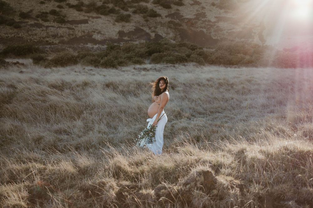 sunset hawaii maternity photoshoot flower bouquet white sheet topless sun flares at mana road in hilo, hawaii