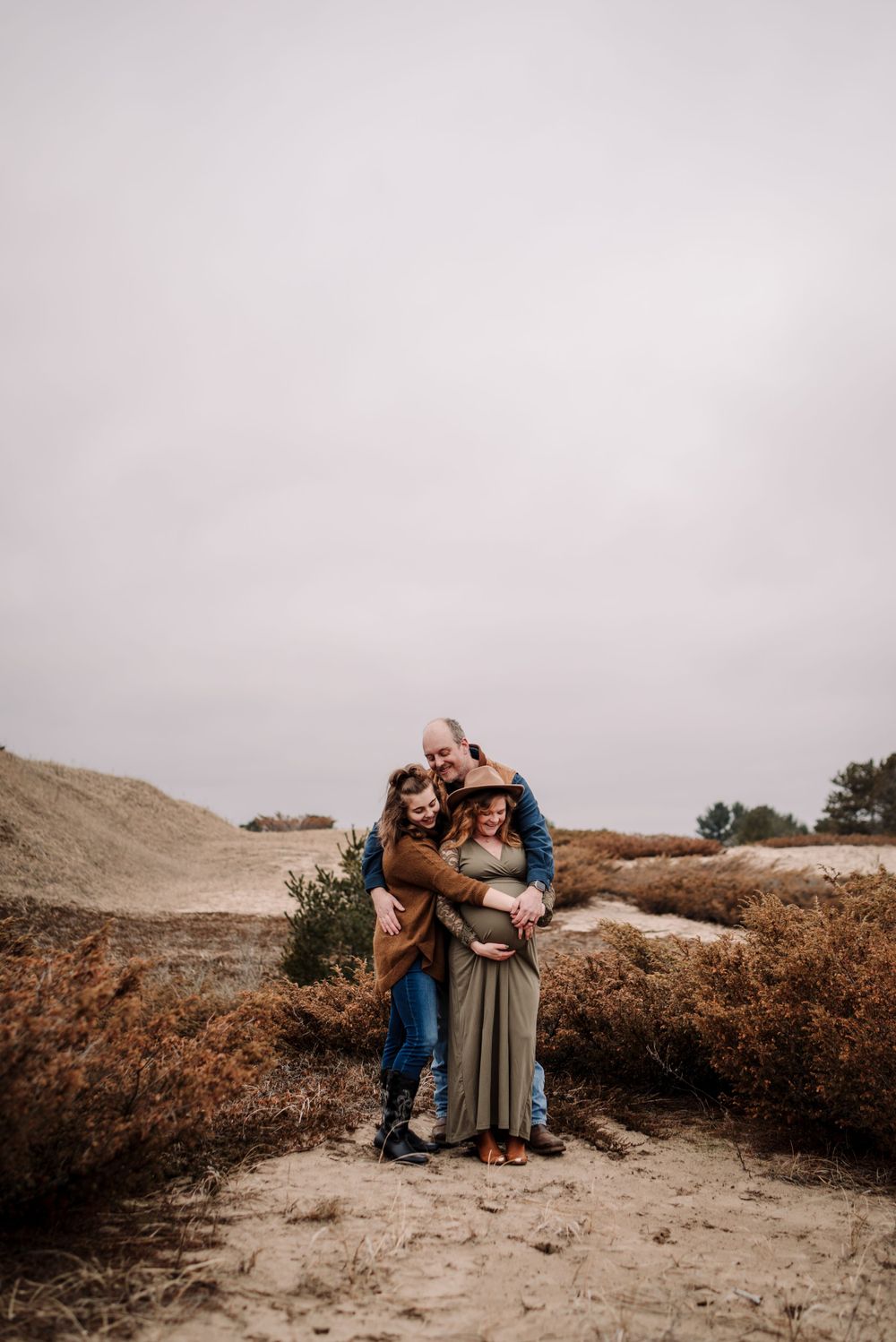 Family portrait session on sandy dunes during golden hour with moody sky.