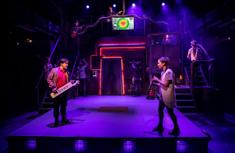 Musicians perform on multi-level stage with neon lighting and digital display.
