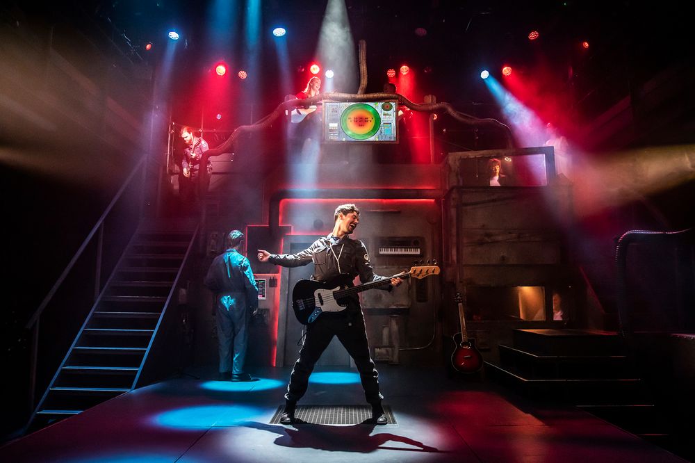 Performer rocking out on stage with dramatic red and blue lighting effects during a theatrical production.
