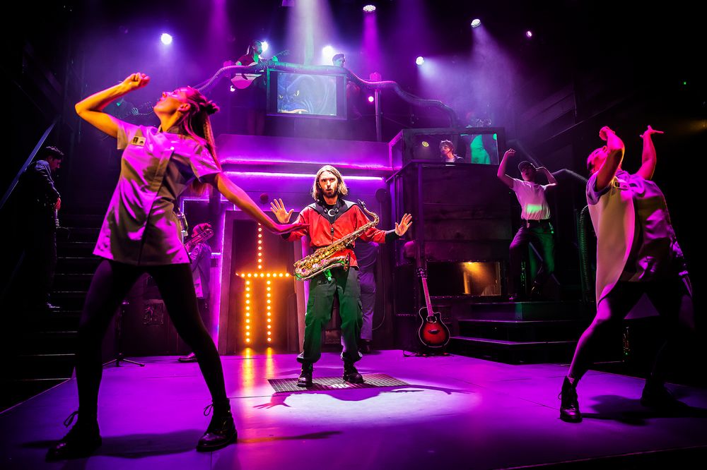 Dynamic stage performance with dancers in dramatic poses under purple theatrical lighting.