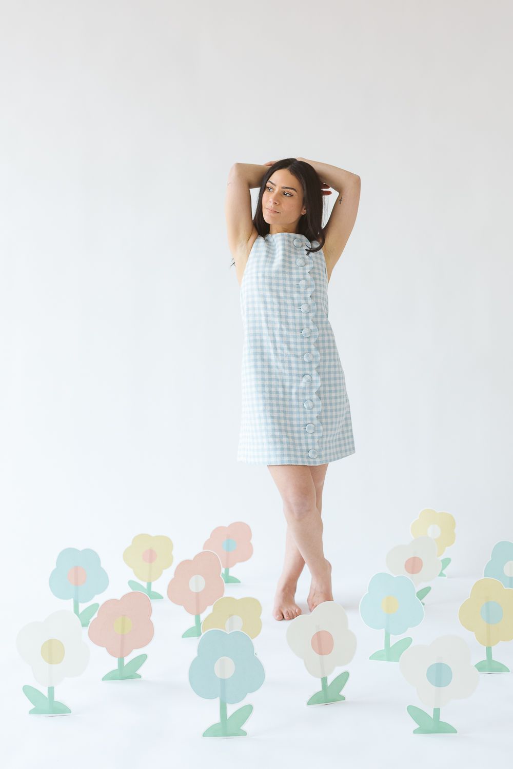a woman wearing a Lisa Marie Fernandez poses with arms behind her head surrounded by paper flowers in multicolors