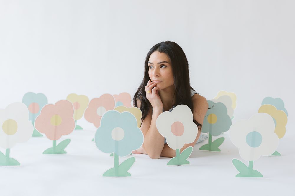 a woman lays down on the floor with paper flowers in multi colors for her branding session by NYC Photographer