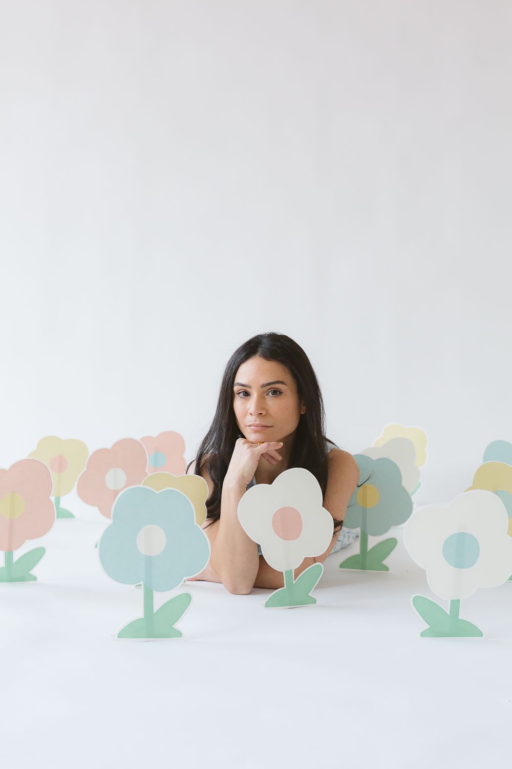 a woman lays down on the floor with paper flowers in multi colors, photo by Paula Ortiz NYC Family Photographer