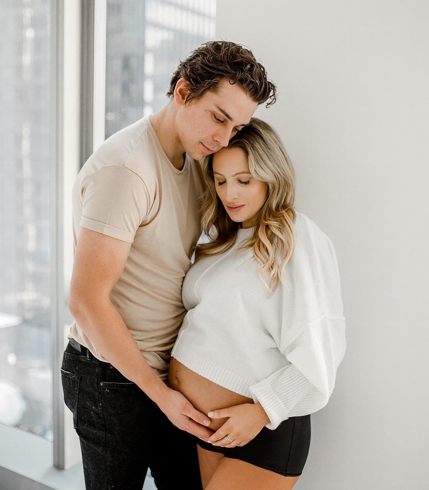 A tender embrace captured in a bright modern apartment with city views through the windows.