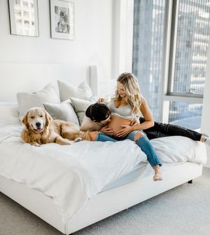 A couple shares an intimate moment on a white bed while their golden retriever rests beside them.