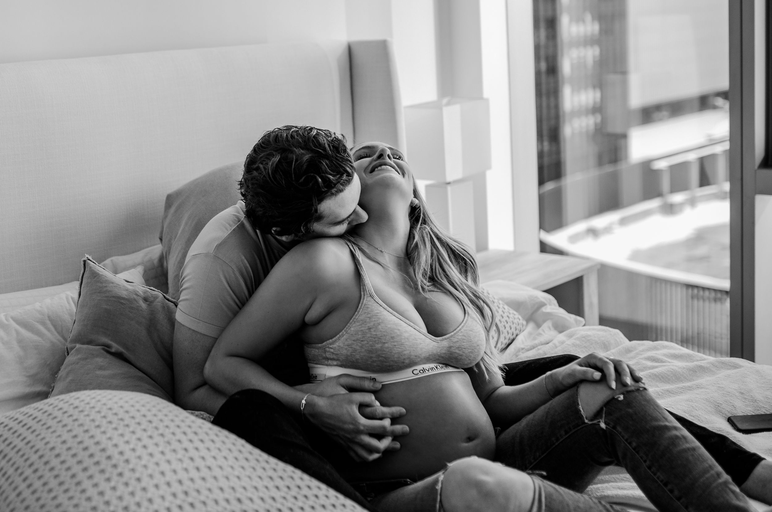 A couple shares an intimate black and white moment on a bed with pillows.