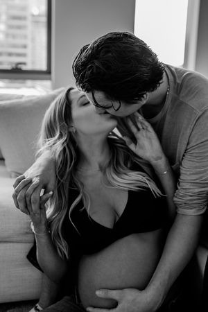 A black and white intimate portrait of a couple sharing a tender moment on a couch.