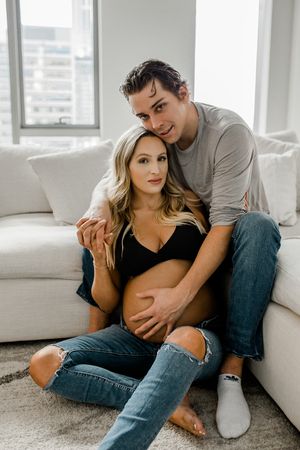 A couple shares an intimate moment while sitting together on a white couch in a modern apartment.