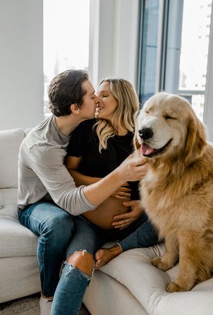 A happy golden retriever joins a couple on a white couch for a sweet candid moment.