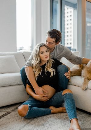 A couple shares a tender moment on a gray couch in a modern apartment with city views.