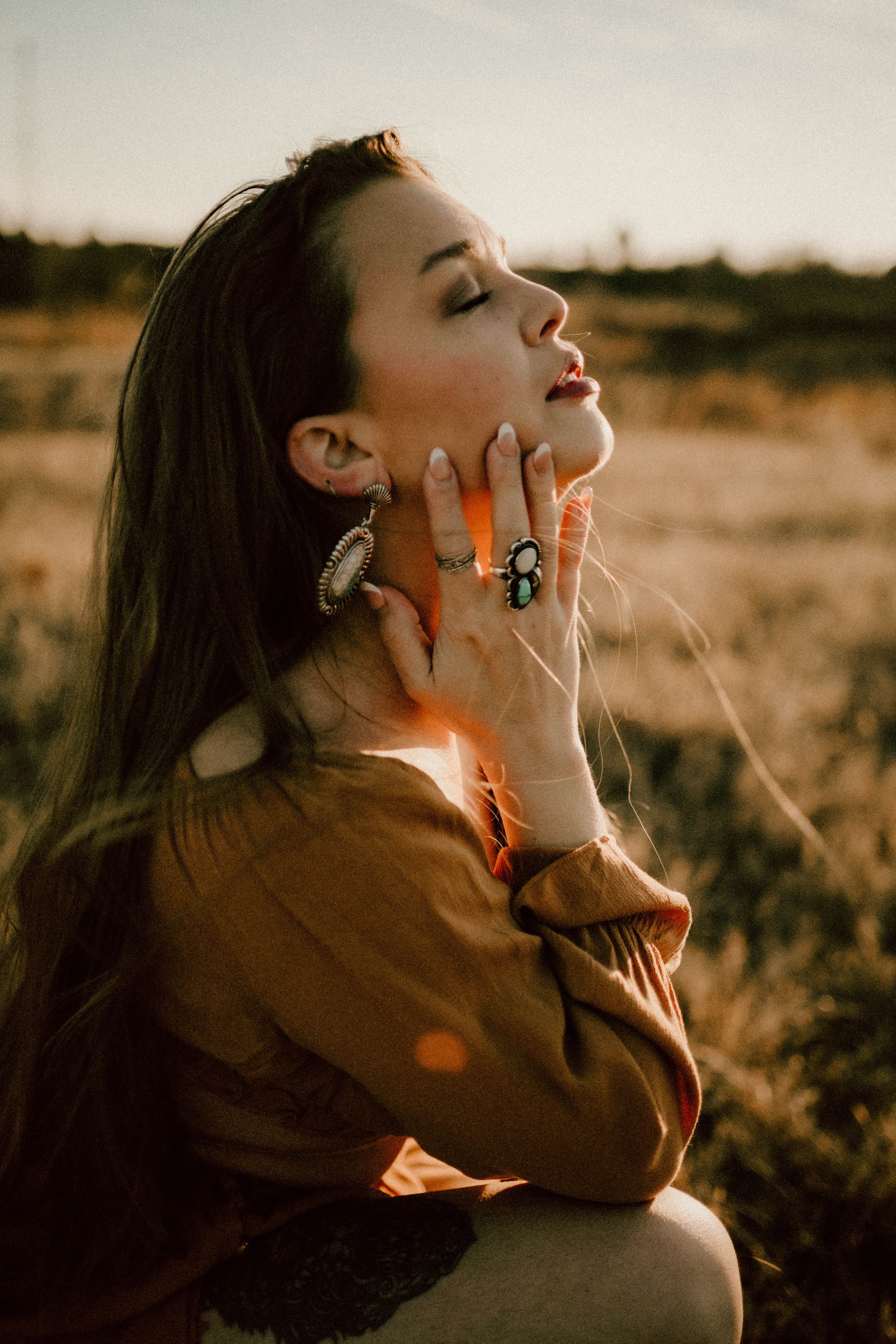 Woman in brown sweater poses in warm sunlight with artistic lens flares.