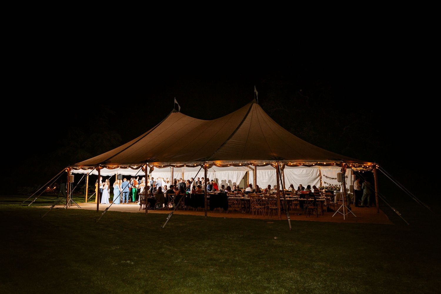 Night photo of teepee lit up with wedding party dancing