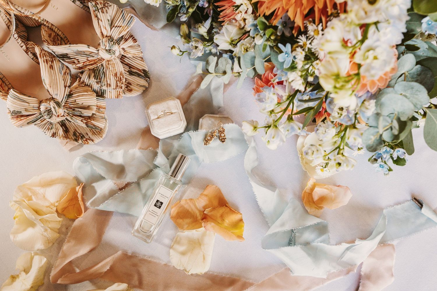 flat lay photograph of bride details showing perfume wedding bands shoes and bouquet coral peach dusty blue