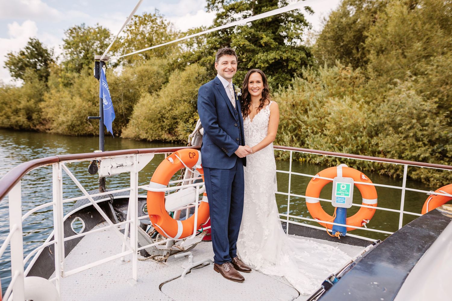 Newlyweds standing together on a boat deck with orange life preservers in the background.