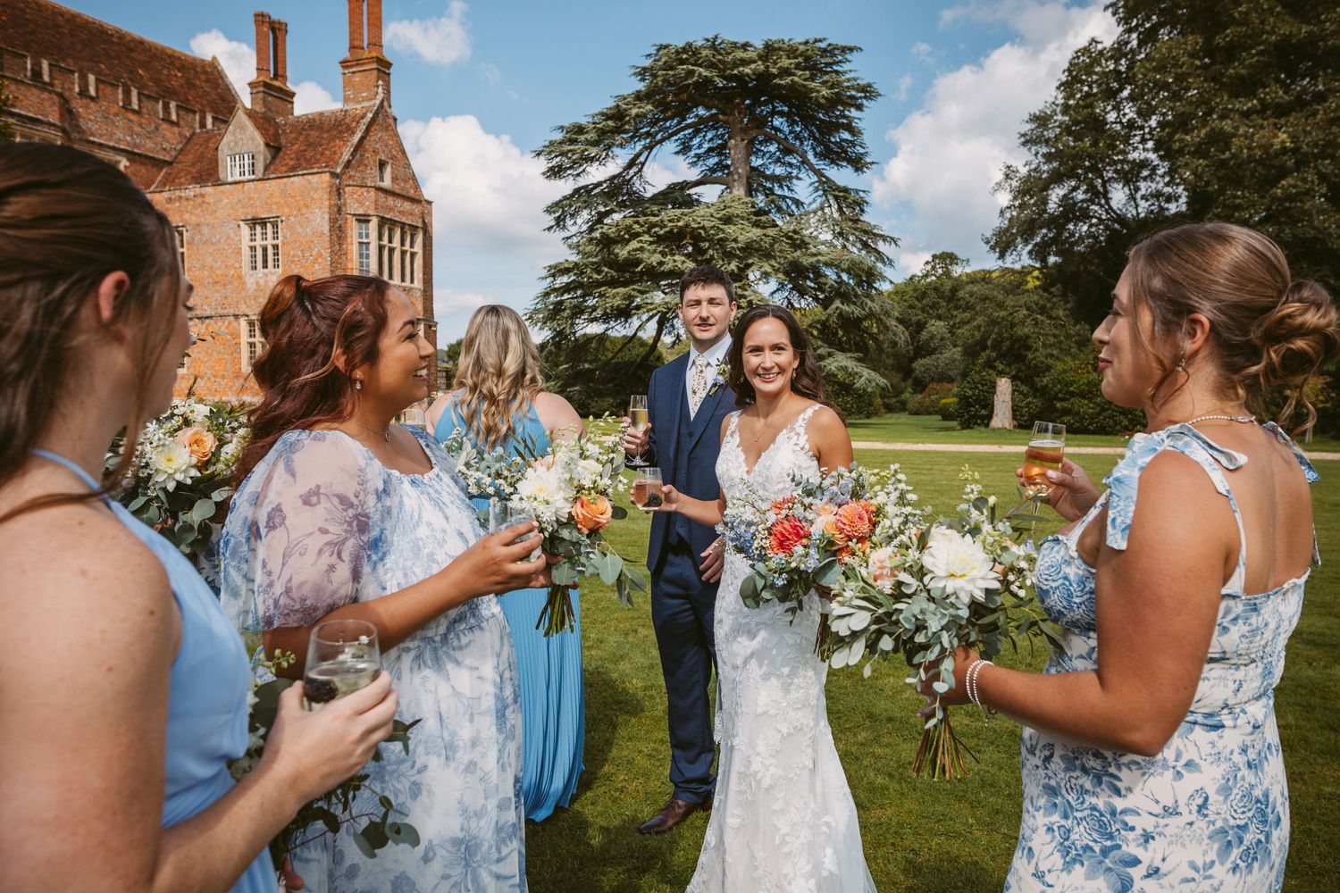 Wedding celebration on the lawn of a historic brick mansion with guests in blue dresses.