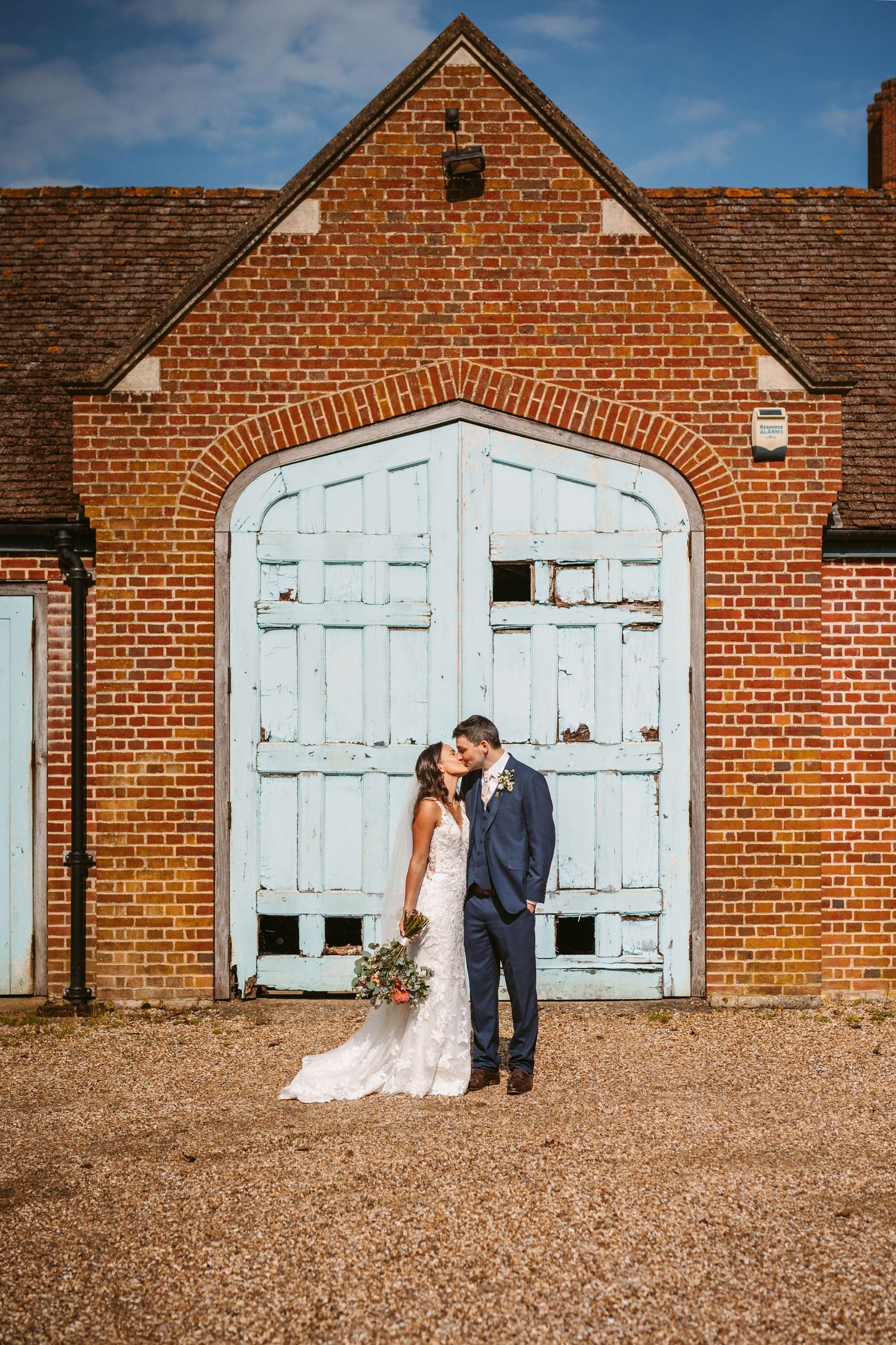 happy newly weds kissing in front of rustic blue painted pretty shaped doors at Mapledurham