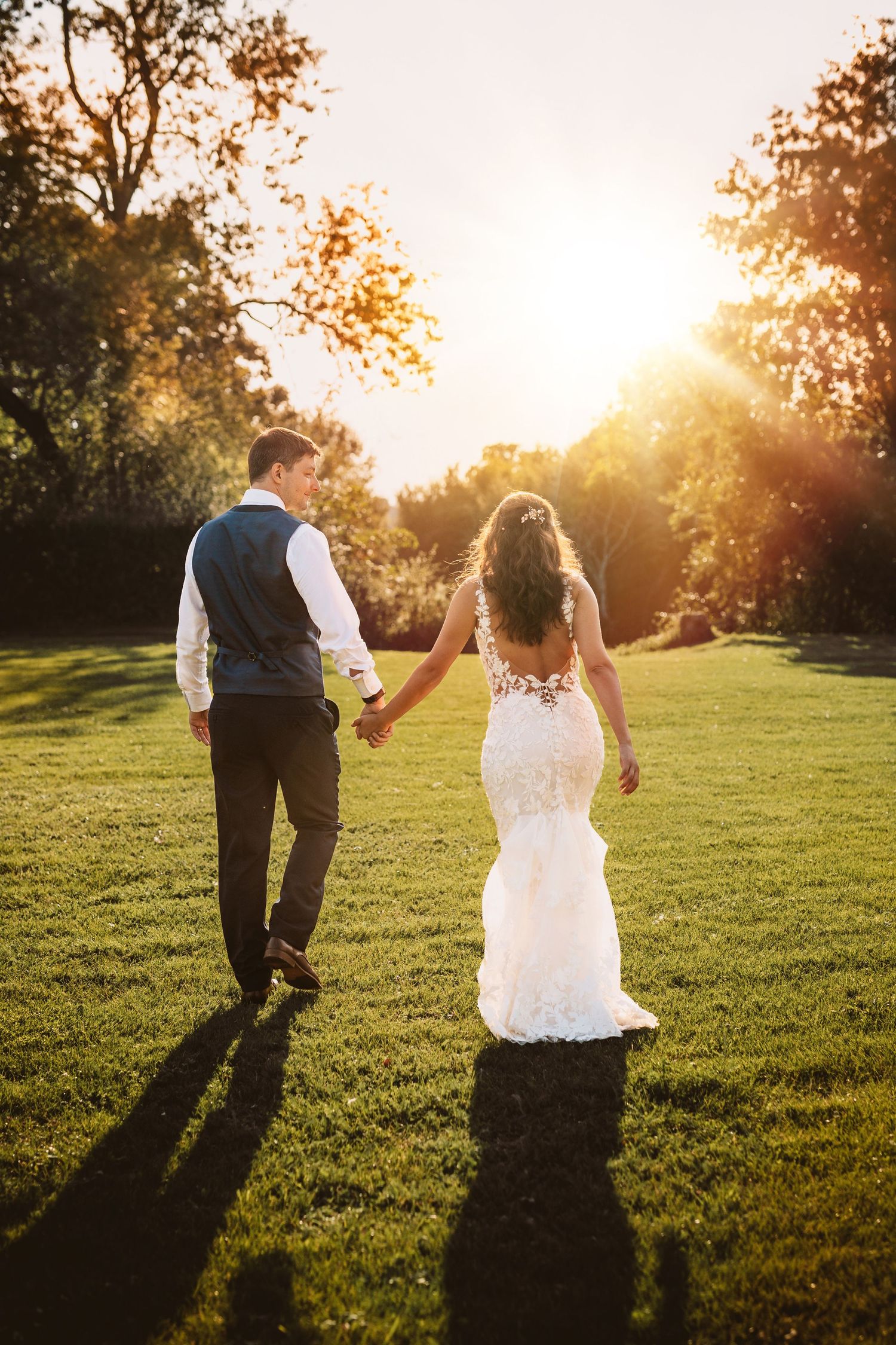Holding hands and walking towards golden sunset happy and in love newly wed bride and groom at Mapledurham