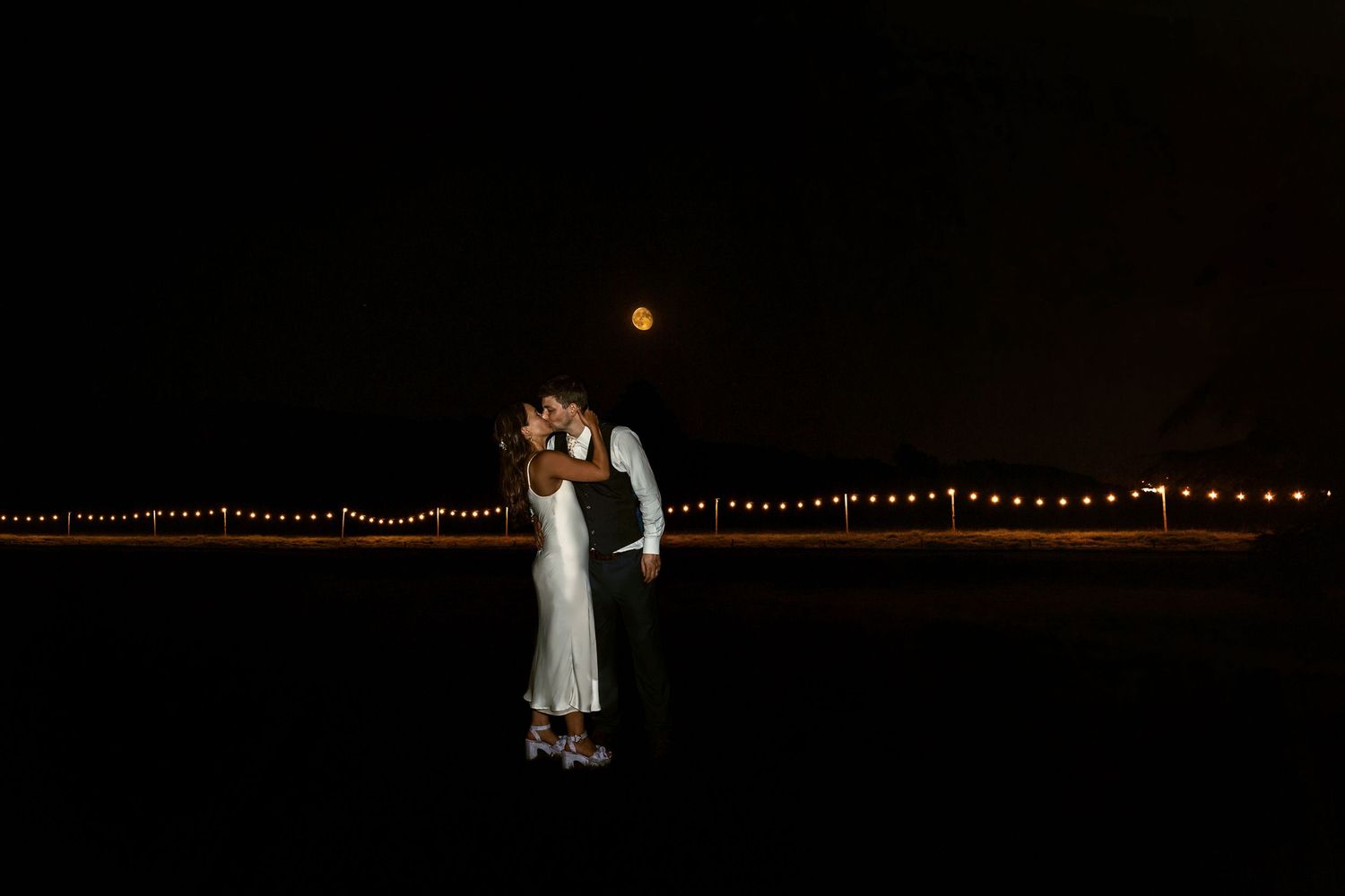 Bride and Groom kissing with full moon in the sky behind them