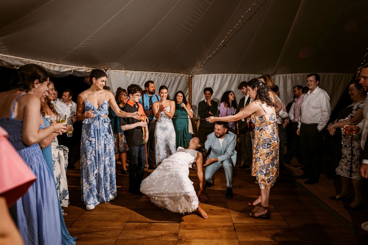 Wedding guests dancing and celebrating on a wooden dance floor under a tent at a reception.