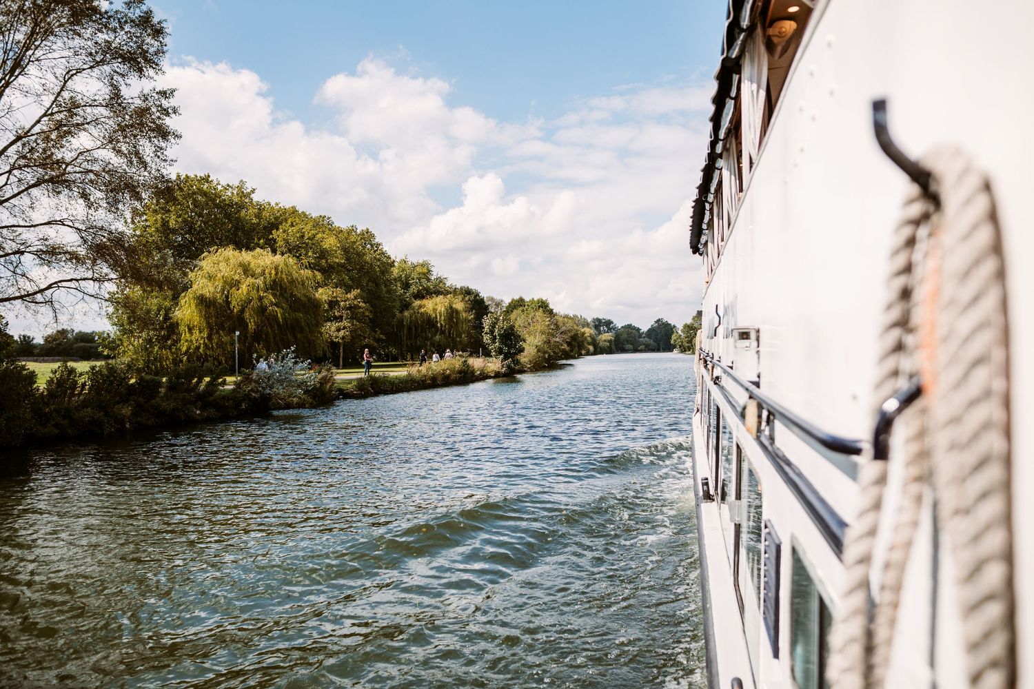 View from boat deck showing peaceful river landscape with trees along shoreline.