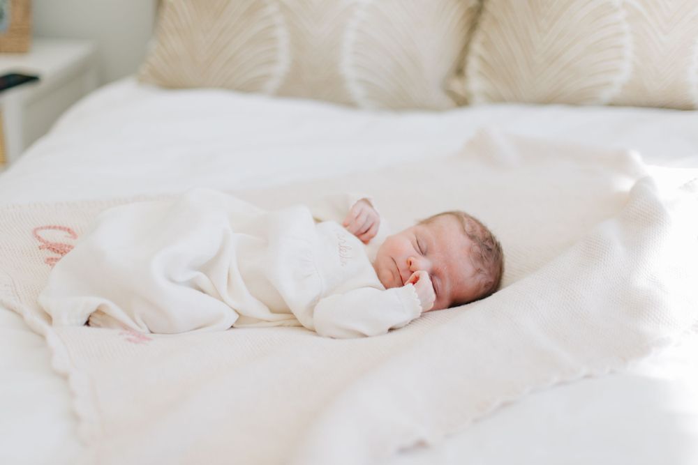 Sleeping newborn baby in white onesie rests peacefully on white bedding.