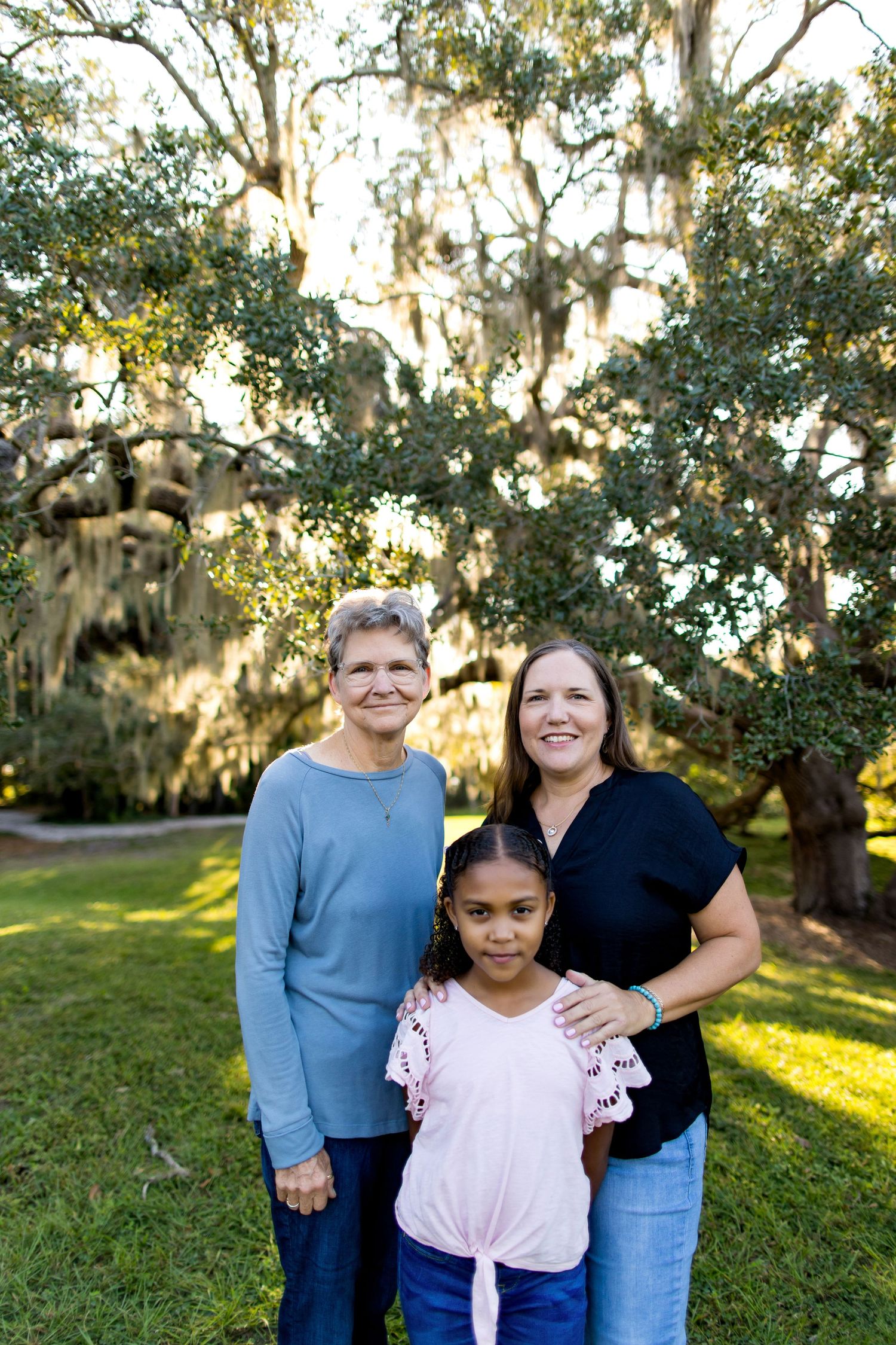 Family portrait outdoors under moss-covered oak trees during golden hour.