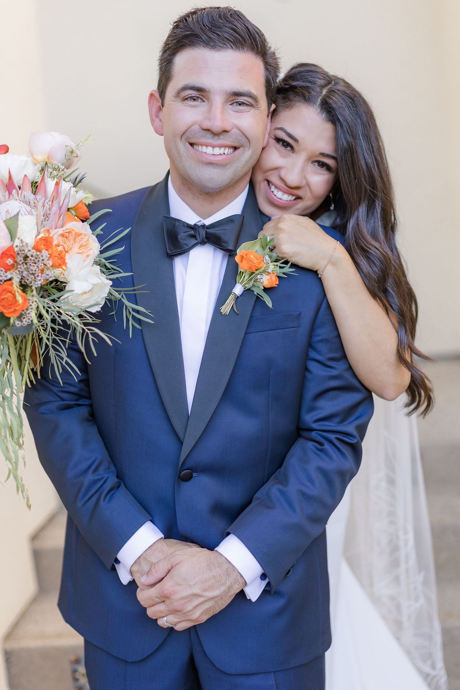 Wife and hubby in blue tuxedo pose wife behind husband