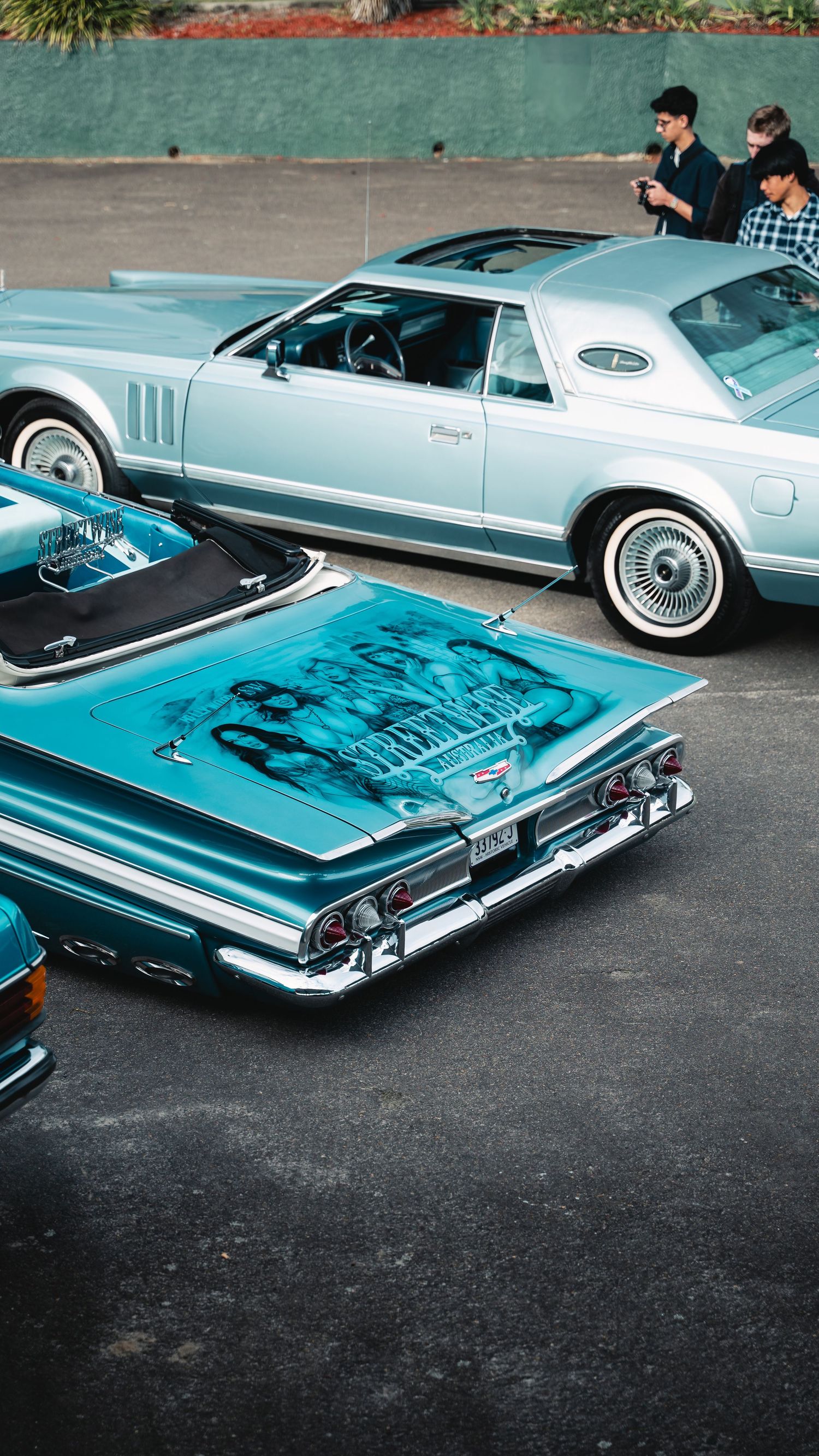 Two vintage lowrider cars with custom paint and chrome details parked at a classic car meetup.