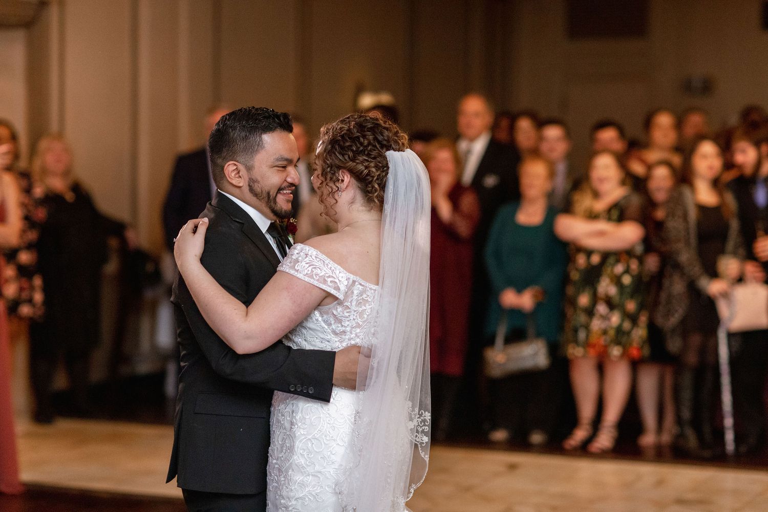 Wedding couple shares their first dance surrounded by onlooking guests in formal attire.