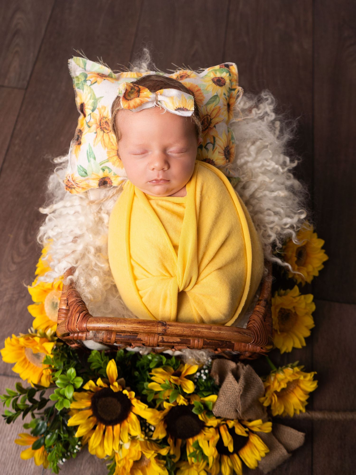 Baby girl sleeping in rattan bed prop, wrapped in mustard yellow, with sunflowers at newborn photoshoot in Doncaster.