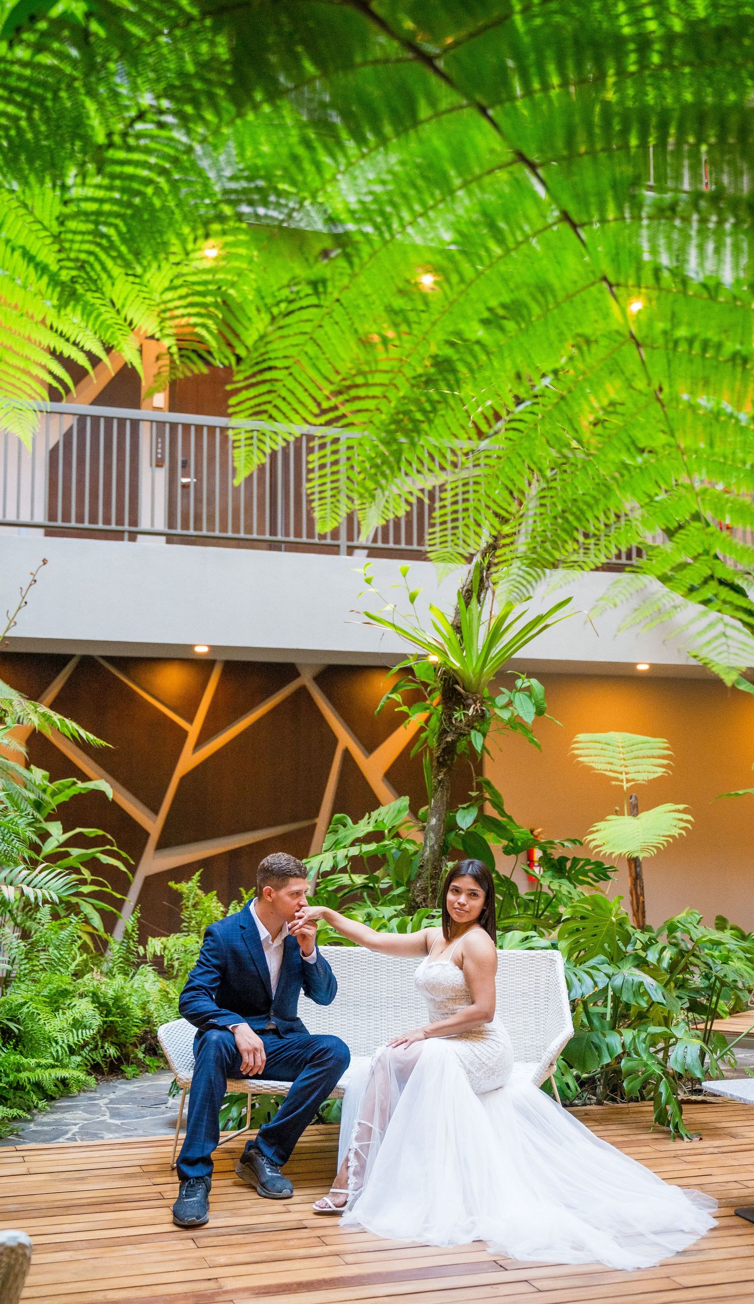 Groom kissing the bride's hand while both are seated in the middle of the courtyard at Botanika Osa Peninsula.