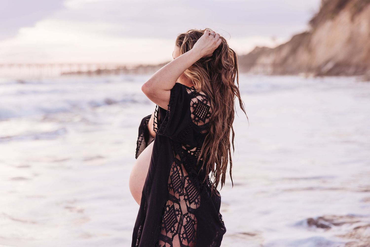 Artistic silhouette of expecting mother against cloudy beach sunset.