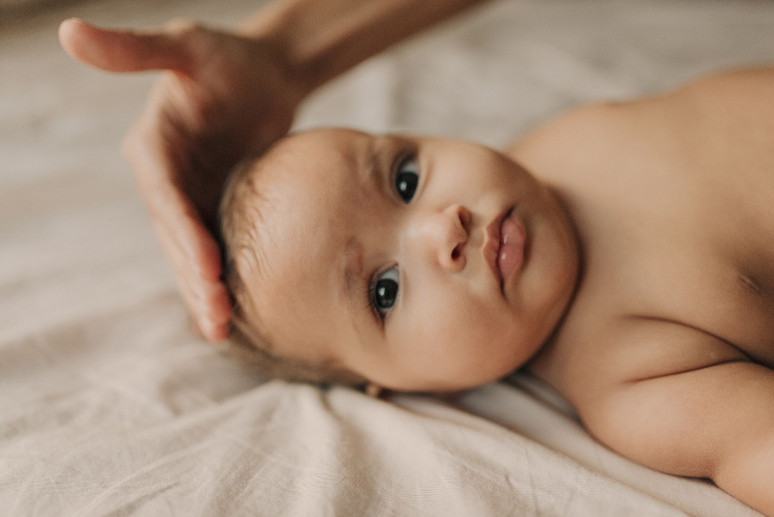 Close-up of an infant lying on white bedding with soft natural lighting.