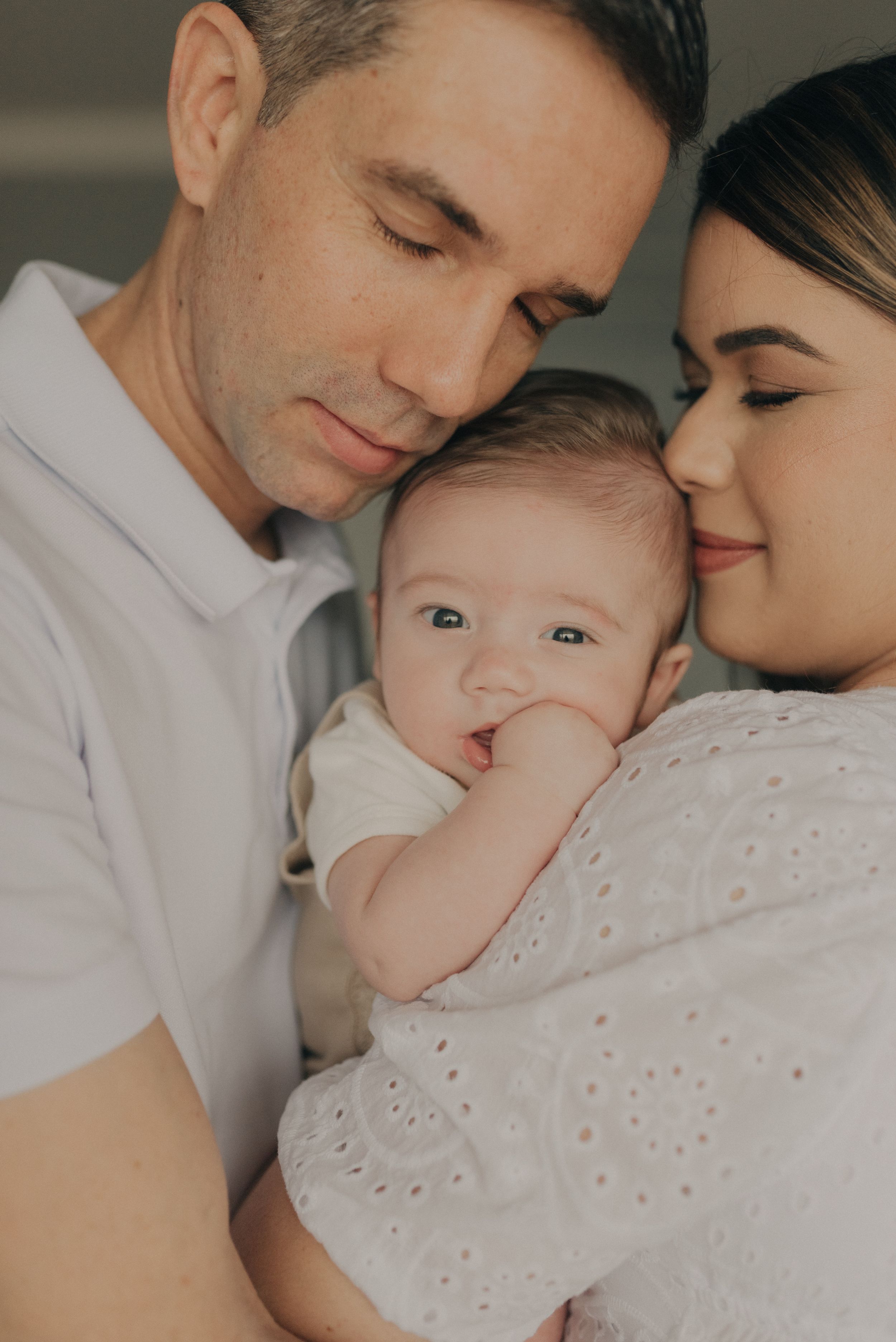 Intimate family portrait with baby in white outfit during indoor photoshoot.