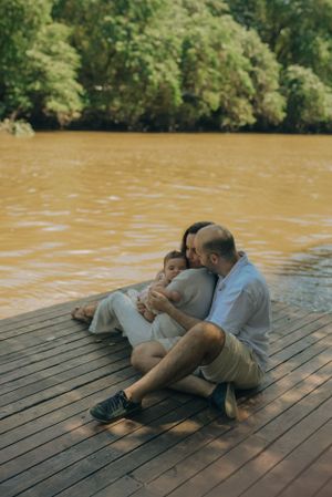 Family relaxing together on wooden dock by peaceful brown river.