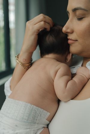Tender moment of parent holding sleeping baby against chest near window.
