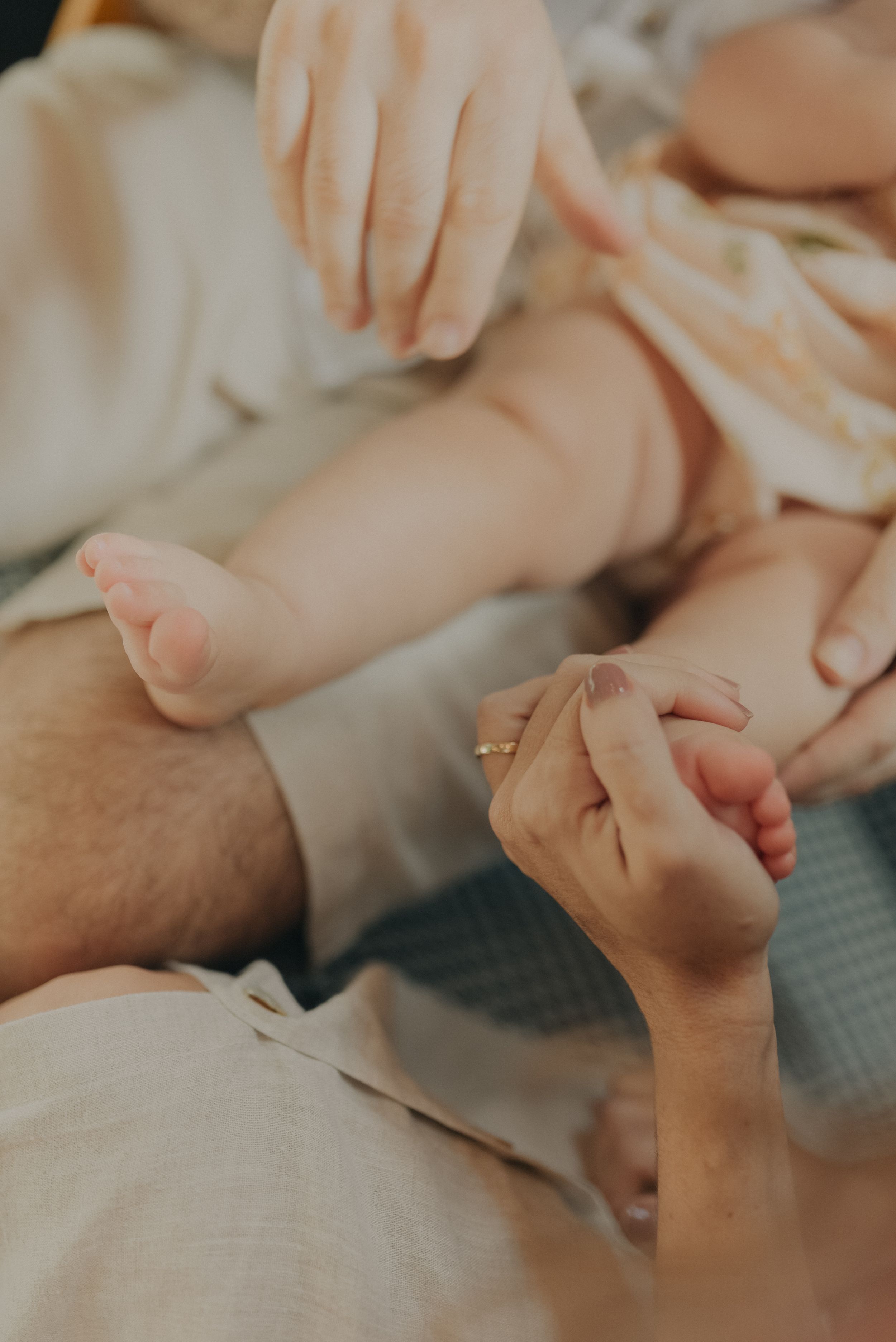 Close-up view of tiny baby feet being gently held by adult hands on a soft blanket.
