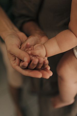 Close-up of adult hands tenderly holding baby's small hands in warm lighting.