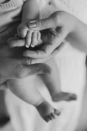 Close-up black and white image of an adult hand gently holding a tiny baby's hand.
